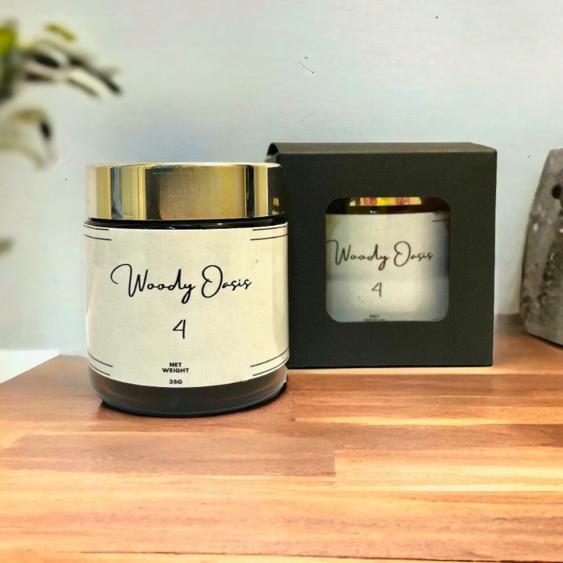 Showing front view of woody oasis bukhoor no.4 in a glass bottle from the front with anther bottle to show the packaging on a wooden table. 